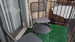 Een balkon met kunstgras, twee rieten stoelen, een klein rond tafeltje en een metalen leuning.