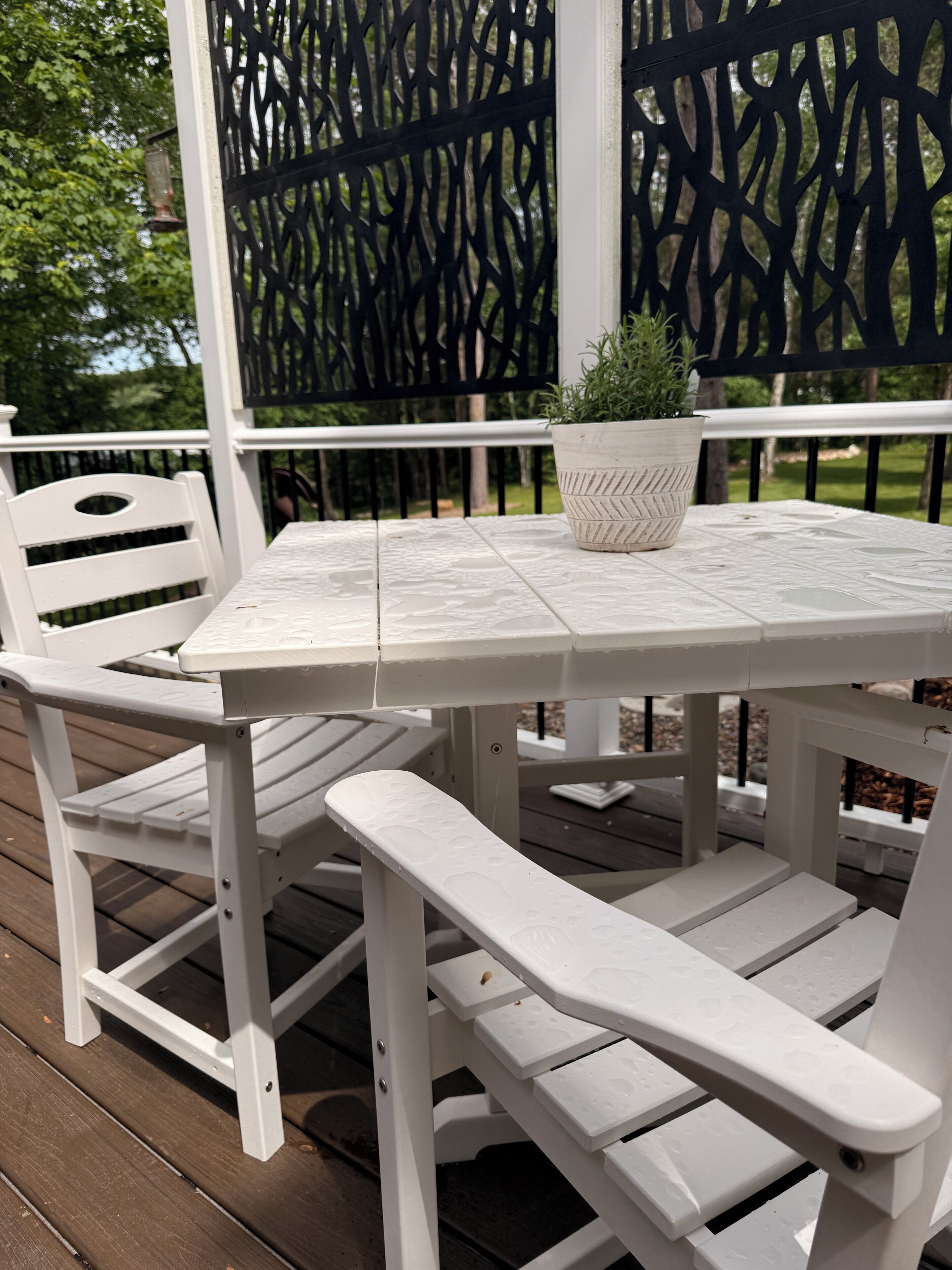 Une table et des chaises blanches destinées à l’extérieur, avec une plante en pot posée sur la table.