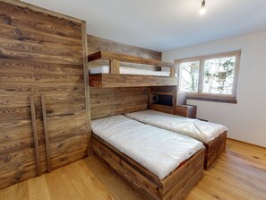 Ein kleines Zimmer mit Etagenbett, Holzwänden, einem Fenster und einer kleinen Sitzecke.