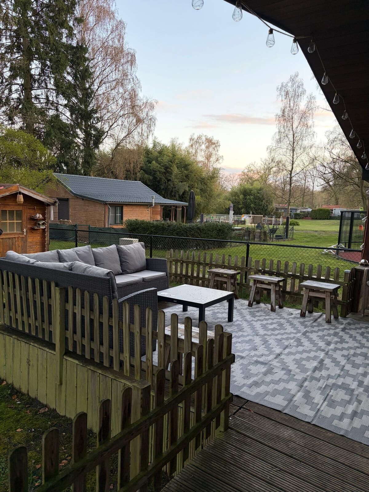 Eine Terrasse mit Gartenmöbeln, einem Holzzaun und Blick auf ein Haus und Bäume.