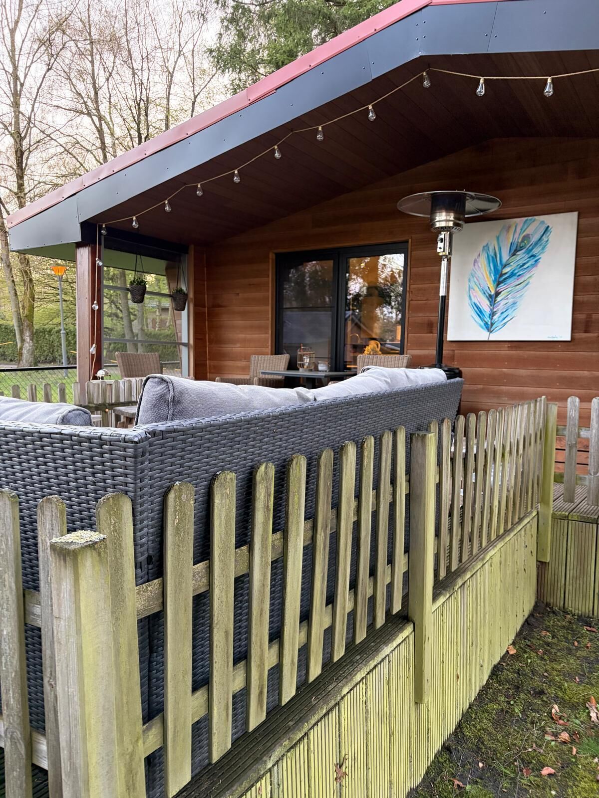 A cozy outdoor seating area with a wicker sofa and a wooden fence.