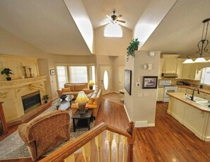 A spacious living area with a fireplace, sofa, and dining table. A kitchen with a sink and cabinets is visible. - Arbour Crest by Grenadier Luxury suites (Calgary)