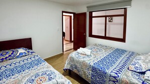 Una habitación con dos camas, una puerta de madera, una ventana con vistas y una lámpara en el techo.