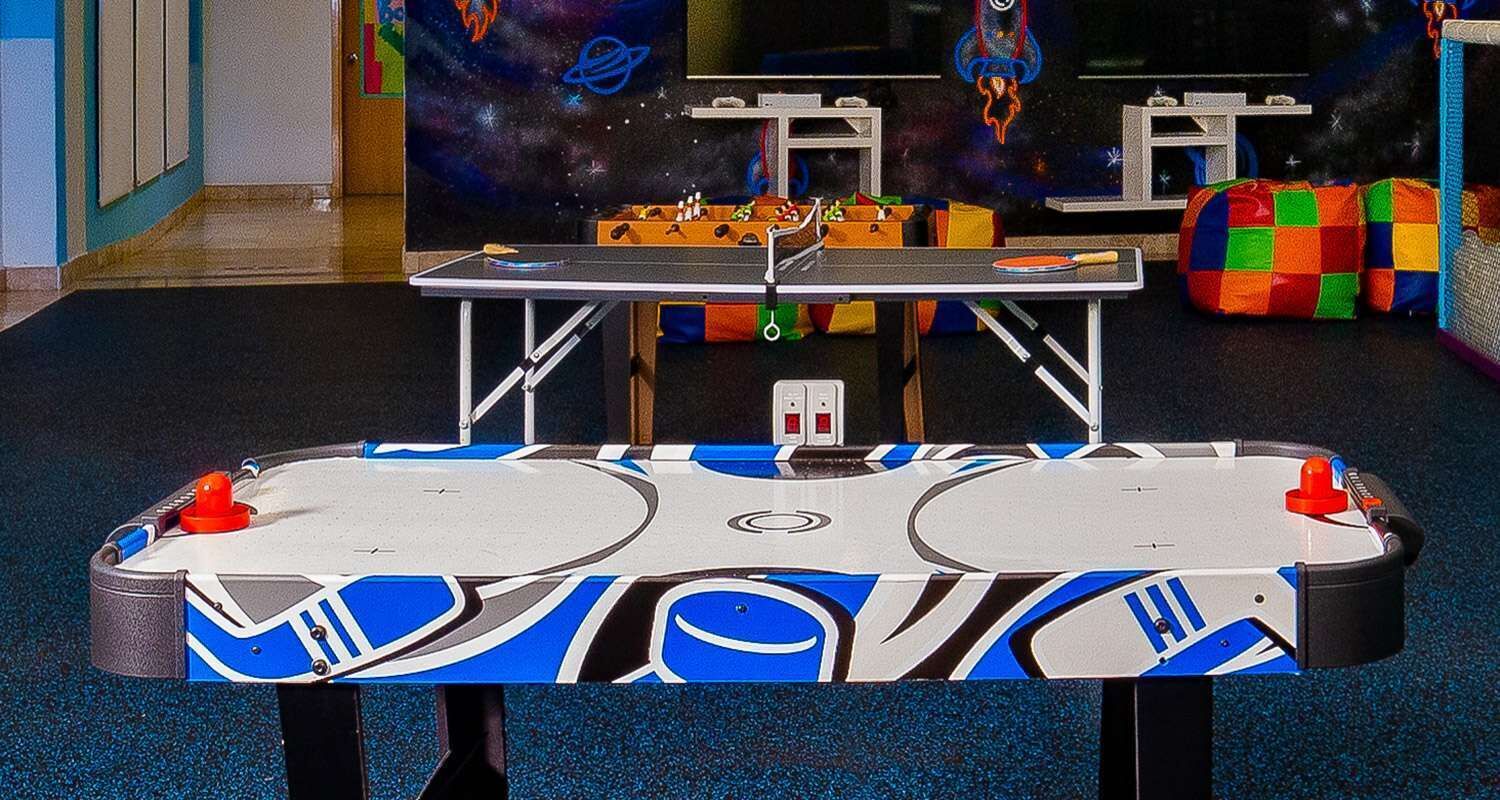 Una mesa de ping pong con diseño temático del espacio, rodeada de pufs de colores y un mural de galaxia al fondo.