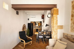 Ein Wohnzimmer mit einer Couch, einem Esstisch mit Stühlen, einem schwarzen Sessel und einer Küche im Hintergrund.