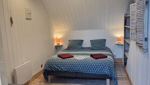 A bedroom with a sloped ceiling, wooden flooring, a bed with patterned bedding, bedside lamps, and a radiator. - Gîte ⭐⭐⭐ - 2 Adults + Baby - 70m² - Face Petit Train - Terrace - Le Crotoy (Le Crotoy)