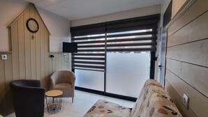 A room with a sofa, a chair, a small round table, a wall-mounted TV, and a sliding glass door. - Gîte ⭐⭐⭐ - 2 Adults + Baby - 70m² - Face Petit Train - Terrace - Le Crotoy (Le Crotoy)