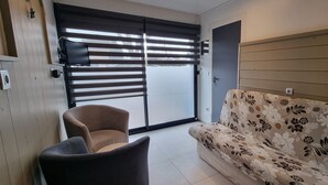 A room with a sofa, a chair, a sliding door, and a wall-mounted TV. - Gîte ⭐⭐⭐ - 2 Adults + Baby - 70m² - Face Petit Train - Terrace - Le Crotoy (Le Crotoy)