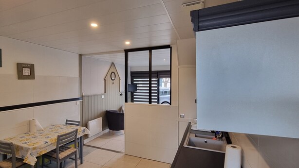 A room with a dining table, chairs, a small black chair, a whiteboard, and a door leading to another room. - Gîte ⭐⭐⭐ - 2 Adults + Baby - 70m² - Face Petit Train - Terrace - Le Crotoy (Le Crotoy)