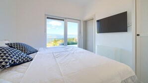 Een slaapkamer met een bed, kussens, een televisie en uitzicht op de omgeving.