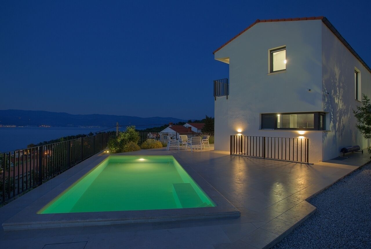 Une maison moderne dotée d’une piscine, d’un balcon et offrant une vue sur la mer.