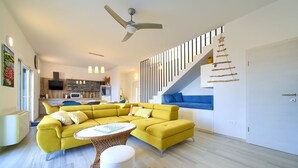 Een moderne woonkamer met een gele bank, een witte salontafel en een trap met blauwe treden.