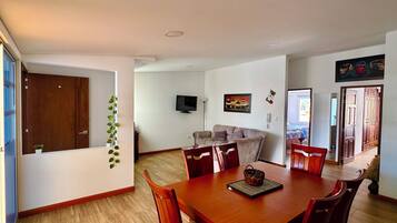 Een eethoek met een houten tafel en stoelen, een bank en een televisie aan de muur.