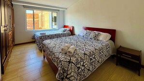 A bedroom with two beds, a wooden wardrobe, a window, and a small bedside table. - Apartment with privileged location in Paipa (Paipa)