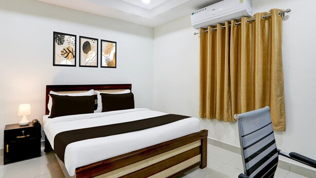 A neatly arranged hotel room with a bed, bedside table, lamp, air conditioning unit, and a chair. - Deluxenest Guest House (Hyderabad)