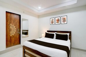Ein Schlafzimmer mit einem Bett, einer Holztür, einem Spiegel und drei gerahmten Blätter-Kunstwerken an der Wand.