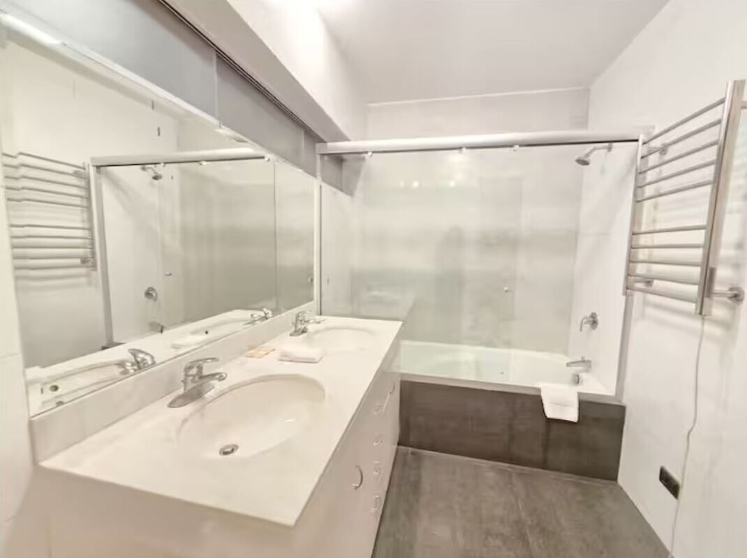 A modern bathroom with two sinks, a glass shower enclosure, and a towel rack.