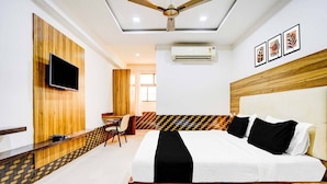 A hotel room with a bed, a desk, a chair, a TV, and an air conditioning unit. - Deluxeinfocity Metro Station Gandhinagar (Gandhinagar)