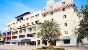 A multi-story building with balconies, a palm tree in the center, and a clear sky. - Deluxeinfocity Metro Station Gandhinagar (Gandhinagar)