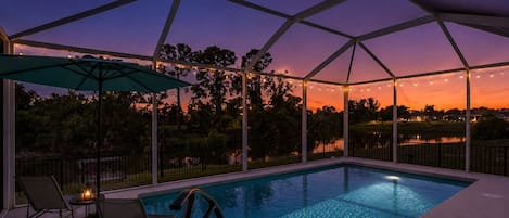 An outdoor swimming pool with a covered area, surrounded by trees and a view of a body of water.