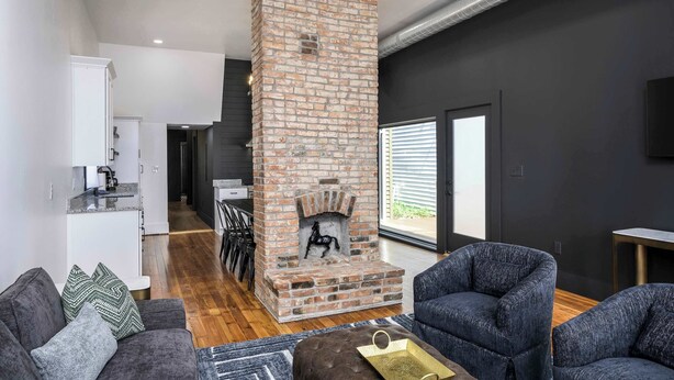 Ein modernes Wohnzimmer mit Kamin aus Ziegeln, dunklen Wänden und einem Essbereich im Hintergrund.