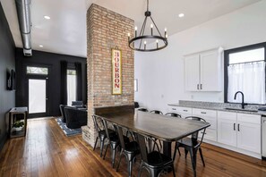 Una cocina moderna con un muro de ladrillo decorativo, una mesa de comedor con sillas, muebles blancos y una lámpara de araña.