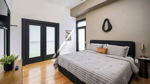Ein Schlafzimmer mit einem Bett, einem Deckenventilator, einer Topfpflanze, einer Tür und einer wandmontierten Lampe.