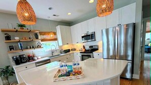 Una cucina moderna con mobili bianchi, elettrodomestici in acciaio inossidabile, un'isola centrale con sgabelli e illuminazione a sospensione.