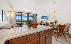 Cocina moderna con una isla grande, comedor con sillas de mimbre y vista al océano.