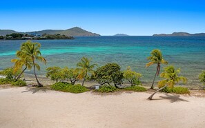 Ein Strand mit klarem türkisblauem Wasser, Palmen und Bergen im Hintergrund.