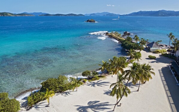 A beach with clear turquoise waters, palm trees, and a distant sailboat. - Oceanfront Sapphire – Water Views, Sleeps 6, Beach (St. Thomas)