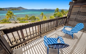 Ein Balkon mit Blick auf das Meer, zwei blaue Stühle und ein kleiner Tisch.