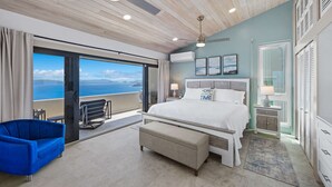 Ein Schlafzimmer mit einem großen Bett, einer Bank, einem blauen Stuhl, einem Balkon mit Blick und einem Deckenventilator.
