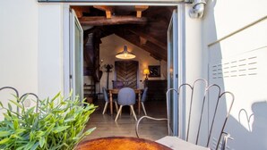 Une porte ouverte donne sur un espace repas comprenant une table et des chaises, un luminaire suspendu et un plafond rustique.