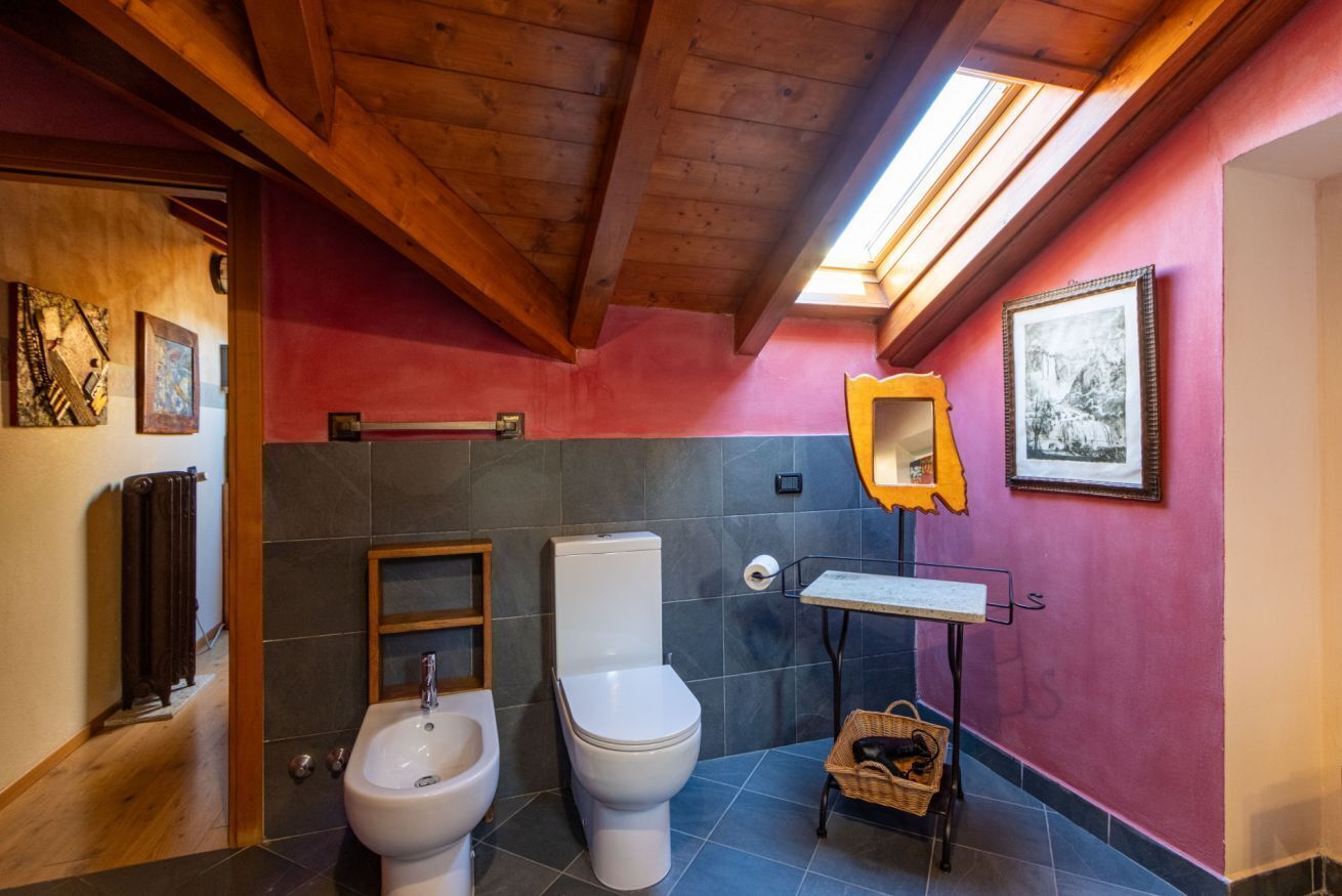 A bathroom with a wooden ceiling, a bidet, a toilet, a sink, and a mirror.