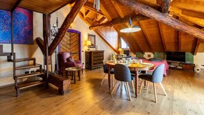 Un loft spacieux avec des poutres apparentes, un coin repas avec une table et des chaises, et un coin salon confortable avec des coussins.