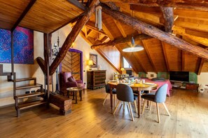 Ein geräumiges Loft mit freiliegenden Holzbalken, einem Essbereich mit Tisch und Stühlen und einer gemütlichen Sitzecke mit Kissen.