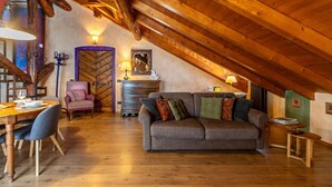 Une pièce mansardée chaleureuse avec un plafond en bois, un canapé, une table à manger avec des chaises et un fauteuil.