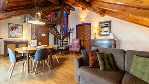 Un intérieur rustique avec un plafond en bois, un coin repas comprenant une table et des chaises en bois, un canapé avec des coussins et une lampe fixée au mur.