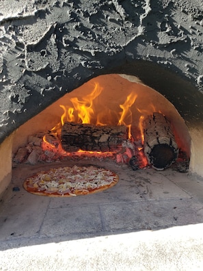 Ein Pizzaofen mit brennenden Holzscheiten, eine Pizza auf dem Boden und eine Steinwand.