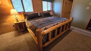 A wooden-framed bed with patterned bedding, a nightstand with a lamp, and a window with blinds.