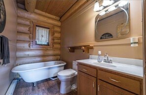 A log cabin bathroom with a bathtub, toilet, wooden cabinets, and a mirror. - The Lodge at Face Lake. Fishing,hiking, and trails. Perfect wilderness retreat. (Logan Lake)