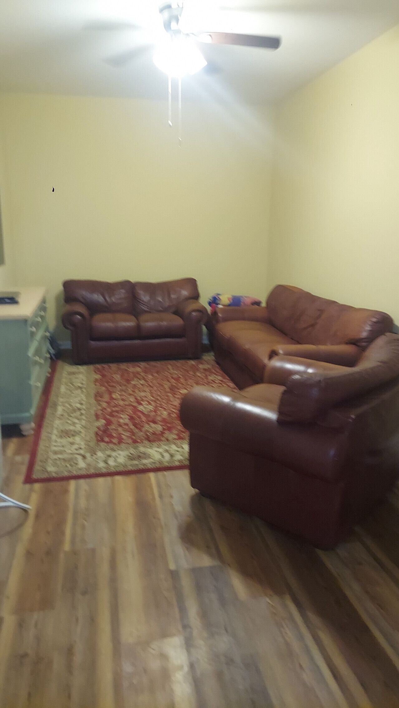 A living room with a brown leather sofa, a patterned rug, and a ceiling fan.