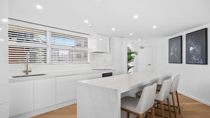 Una cocina moderna con armarios blancos, una isla de mármol e iluminación empotrada en el techo.