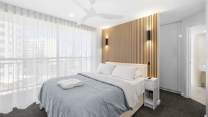 Una habitación de hotel moderna con una cama grande, un ventilador de techo, una pared de acento de madera y vistas a través de cortinas translúcidas.