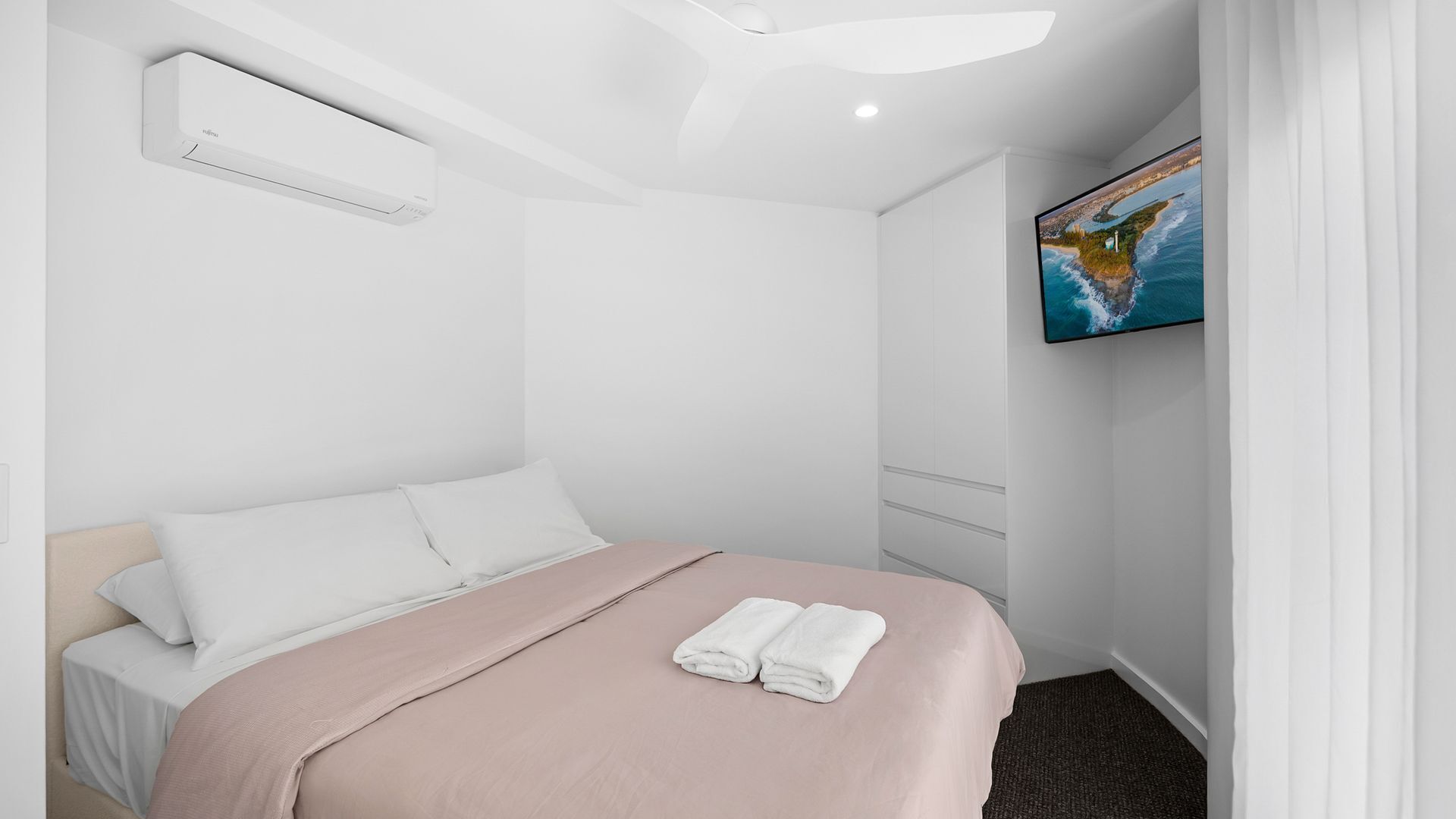 A hotel room with a bed, a wall-mounted air conditioner, a painting, and a carpeted floor.