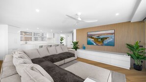 Una sala de estar moderna con un sofá seccional, un televisor de pantalla plana montado en una pared de madera y un ventilador de techo.