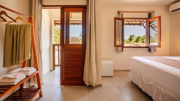 A hotel room with a bed, a window with a view, a wooden door, and a towel rack.