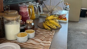 A breakfast setup with a variety of food items and drinks on a table, a window with a view of palm trees, and a covered outdoor area.