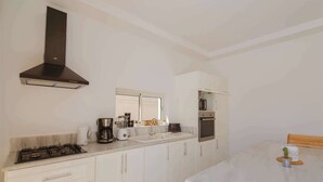 Een keuken met een gasfornuis, koffiezetapparaat, magnetron, oven en witte kasten.